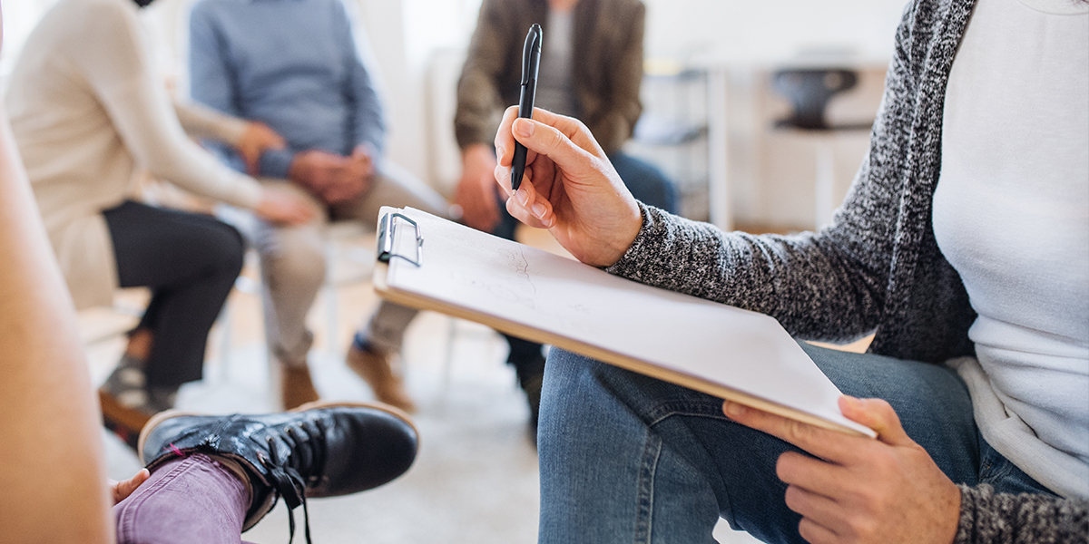 woman fills out form as she sits in circle therapy session A New Outlook Recovery Services
